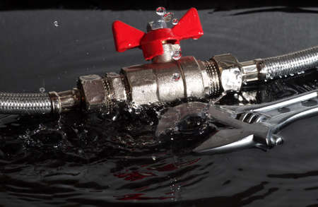 assembled flexible fittings, ball valve, union and adjustable wrench in water with falling drops and waves, black background, suitable for header or bannerの写真素材