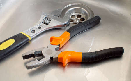 plumbing tools adjustable wrench and pliers in a wet sink, closeup
