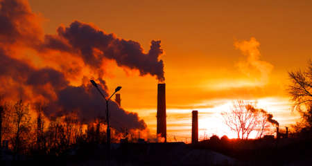 Smoking factory chimneys in morning back lighted by rising sunの写真素材
