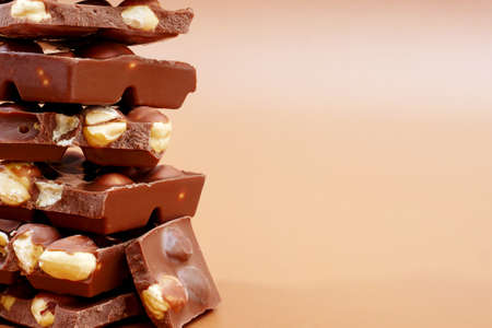 closeup of milk chocolate pieces with hazelnut on brown background with copy space