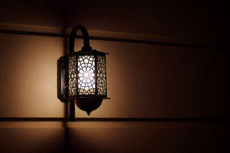 Retro style black lamp on yellow wall. Lamp illuminating wall in the darkness.