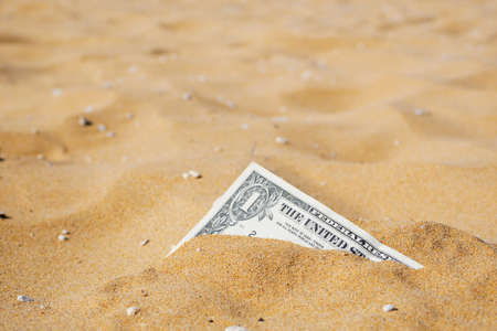 Closeup of one dollar banknote corner buried in the sand. Copy space.の写真素材