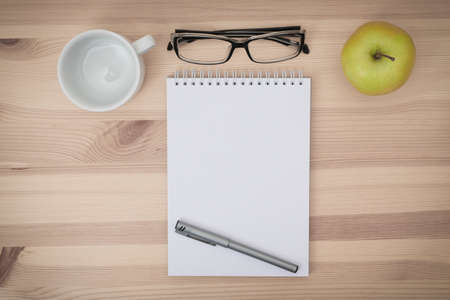 Work space: sketchbook, eyeglasses, coffee cup, green apple and pen on wooden desktop. Top view ,...