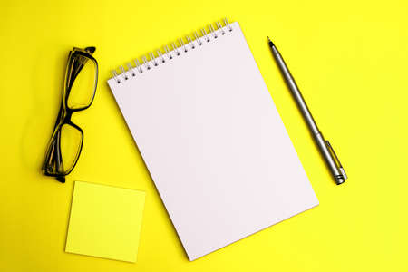 Top view on sketchbook and pen with eyeglasses on yellow backgroundの写真素材