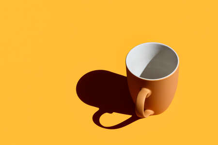 Empty brown coffee mug with hard shadow on yellow background with copy spaceの写真素材