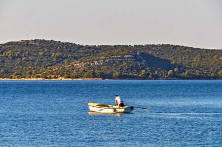 A young man practicing rowing in a traditional boat early in the morning, facing away from the viewerの写真素材