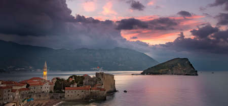 Sunrise over Budva old town with lit tower of Sv. Ivan church, old town's citadel and island Sv. Nikola to the right. Picturesque mountains and coast in backgroundのeditorial素材
