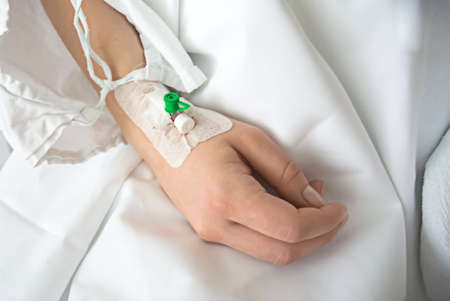 Close up of a intravenous drip in patient's hand in hospital on white sheetsの写真素材