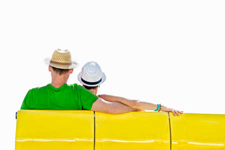 Couple on white background, facing away from viewer, Caucasian, sitting on yellow bench, both wearing hats and summer clothes, isolatedの写真素材