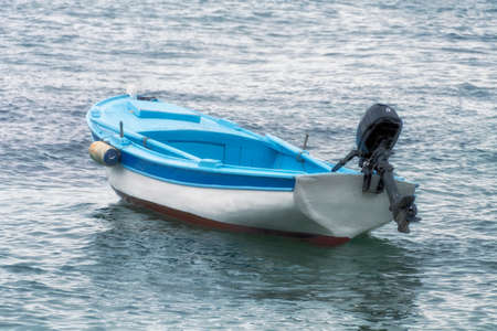 Small fishing boat painted in blue and white with paddles and small outboard engineの写真素材