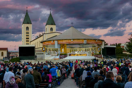 MEDJUGORJE, BOSNIA AND HERZEGOVINA, October 04 2016. Thousands of pilgrims attending a holy mass/service in the evening. Dramatic blue and purple clouds and sky behind the Saint James church.のeditorial素材