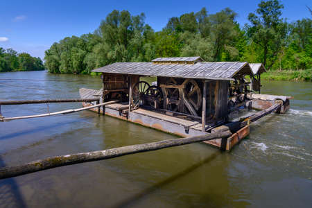 Traditional vintage mill on Mura river, Slovenia. The mill is floating on boats and tied to river bank and is powered by a water wheel from river water flowing beneath.の写真素材
