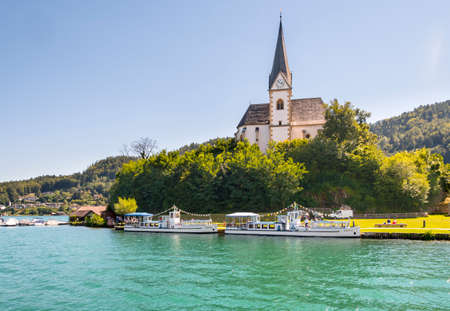 Maria Worth, Austria - August 14 2016: Vintage tourist boats at the church of Maria Worth waiting for passengers. Saints Primus and Felician Church in the background is popular pilgrimage site.のeditorial素材