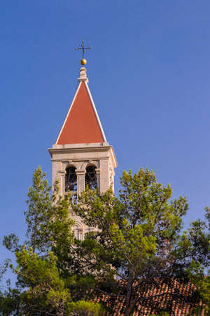 Christian church steeple in front of pines on blue sky with red roof and cross on topの写真素材