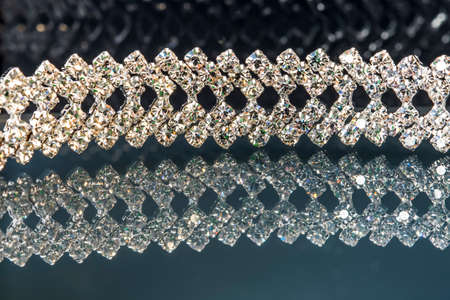 Glittery jewelry - diamond bracelet on a black background with reflections in green and blue color, dark reflective background and surface, close up macro shotの写真素材