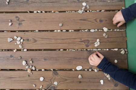 Top view of childs hands playing with stones on woodden bench, desk outdoors at playground, closeup,...