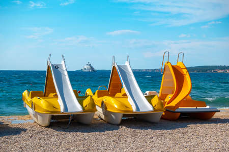 Colorful pedal boats, pedolinos on beach, yellow color, boat with slide, sea in the backgroundの写真素材