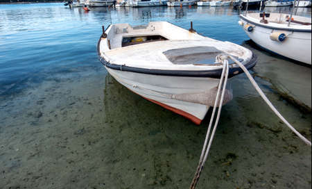 Small traditional wooden fishing boat in harbor, moored to the pier, sky reflecting in water, small water vesselの写真素材