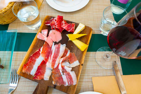Italian style cold meat plate with cheese on wooden board with pancetta, Prosciutto, cheese and mortadella on table with glass of red wineの写真素材