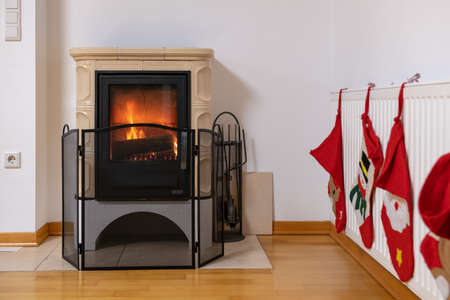 Tiled stove with fire burning inside, cosy and warm interior scene, heating in winter, Christmas decoration on the wallの写真素材