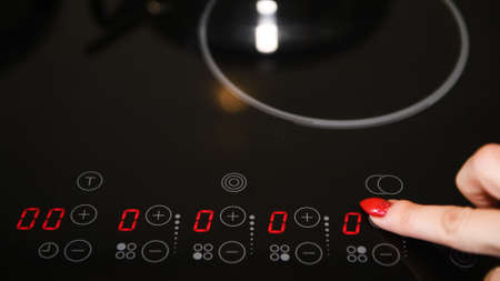 Female finger operating electric stove, nicely manicured finger nails, red polish, LED indicators illuminatedの写真素材