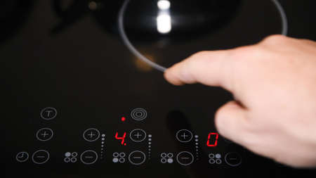 Close up of electric stove control panel, male finger pressing buttons, red LED indicators switched onの写真素材