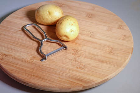 Potatoes on wooden board with a vegetable peeler, close up, isolatedの写真素材