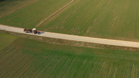 Aerial view of a red tractor and trailer carrying a load of manure on road, agriculture, fertiliying and treating soilの写真素材