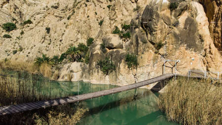 suspension bridge over a river with a rocky mountain landscapeの写真素材