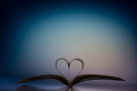 Open book with two paper sheets making a heart shape with a colored backgroundの写真素材