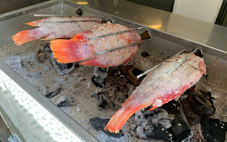 A preparation of grilled red snapper fish in Thai food restaurant with charcoal on stove.