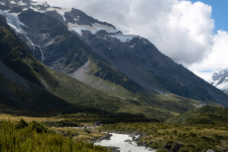 A beautiful breathtaking scene of a massive mountain with a small fresh river melting from glacier near the trekking route at Mount Cook National Park, New Zealand.の写真素材