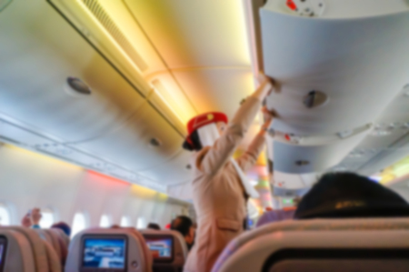 Blurred background of  interior aircraft , flight attendant helping passenger to put luggage cabin compartment.の写真素材