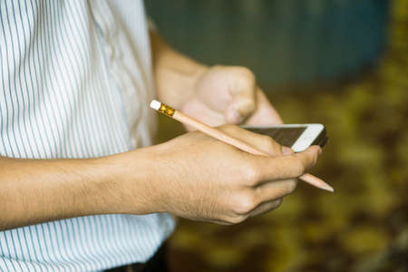 business man use contact information from mobile to contact his client,businessman use smartphone in office and holding pencil,selective focus,vintage color.の写真素材