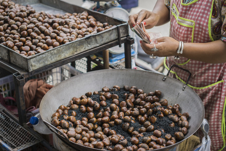 women sell roasted chestnuts to buyers in the market,Sweet chestnuts, Castanea sativa, on a hessian sack was sale in Thailand street market,selective focus.の写真素材