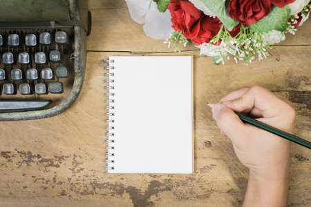 Note book paper on wooden,Blank note book ,Laptop and  Typewriter,roses with hand working on old wooden table, valentine,business concept,Vintage tone,selective focus.can be used for display.の写真素材