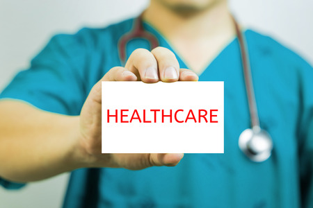 Doctor holding a  business card with capital lettering HEALTHCARE in hand,Doctor shows empty card.Medical concept,Closeup shot of a young doctor showing abusiness card, Selective focus.vintage tone.の写真素材