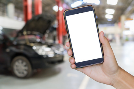 closeup of man with broken car and smart phone, Man hand holding mobile smart phone , tablet,cellphone over Blurred of car technician repairing the car in garage background.の写真素材