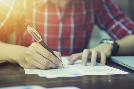Close-up Of Businessperson Signing Contract,Man writing paper at the desk, man writing with pen and reading books at table,man Signing, Contract, Form. in office ,morning light ,selective focus.の写真素材