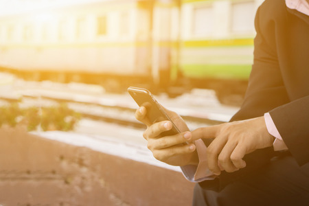 young man sitting with mobile phone waiting for train,businessman holds smartphone with searching for free wifi in train station. student with smartphone in subway,selective focus,copy,vintage colorの写真素材
