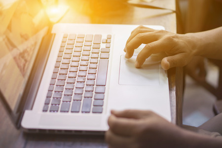 Hand on touchpad of laptop in back light,Man using touchpad on notebook with his finger, toned with sunlightusing,gadgets recreation time in coffee shop,vintage color,selective focus.の写真素材