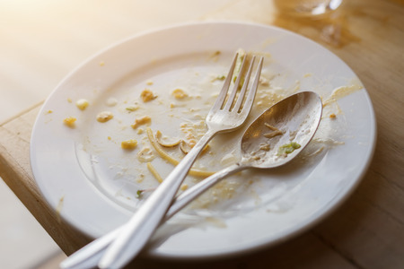High angle view of dirty white plate with fork across it on wooden table background,vintage colorの写真素材