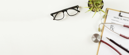 Top view of modern, sterile doctors office desk. Medical accessories on a white background with copy space around products.Workplace of a doctor. Stethoscope, clip board, glasses and other thingsの写真素材