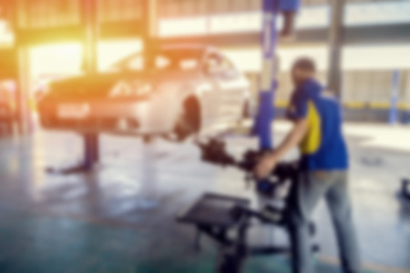 Blurred background of car technician repairing the car in garage,mechanics fixing car in a workshop background,car suspension detail of lifted automobile at repair service station,vintage color.の写真素材