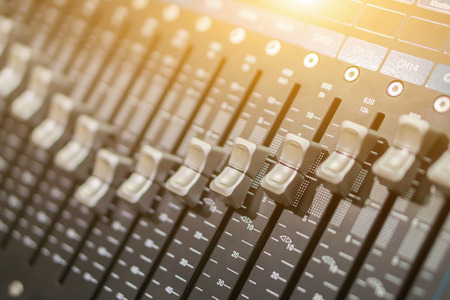 Side closeup on a sliders of a mixing console. It is used for audio signals modifications to achieve...