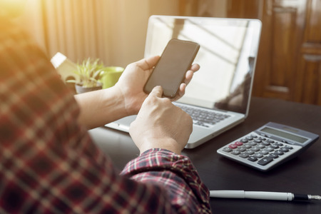 Side view shot of a man's hands using smart phone in interior, rear view of business man hands busy using cell phone at office desk, young male student typing calculator at wooden table, flareの写真素材