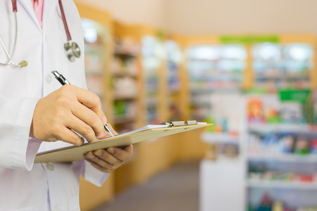 male doctor with stethoscope holding clipboard and writing a prescription,pharmacist writing on prescription clipboard at the hospital pharmacy,Healthcare and medical concept,selective focusの写真素材