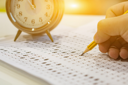 A pencil sitting on a test bubble sheet and alarm clock, optical form of an examination,Answer sheet with pencil,Standardized test form with answers bubbled and a black pencil,selective focus,vintageの写真素材