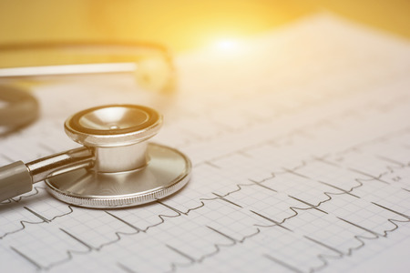 doctor workplace with a stethoscope at wooden table,Cardiogram chart with medical stethoscope and on table closeup,for Surgeon doctor Medical heart,selective focus,vintage color.morning lightの写真素材