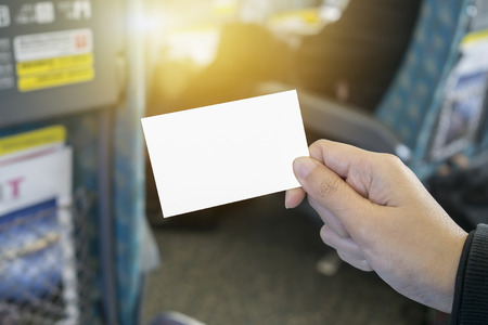 Hands holding a white business visit card, gift, ticket, pass, present close up on blurred of train station,subway,People wait for train on platform background.Copy space,selective focus,vintage colorの写真素材